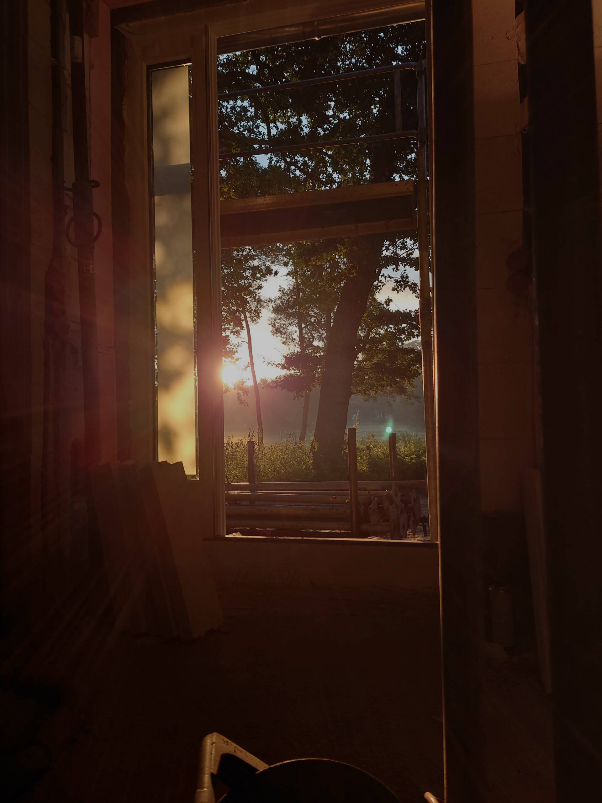 Neubau (8) Blick aus einem Rohbaufenster in eine morgendliche Landschaft mit Sonnenaufgang.