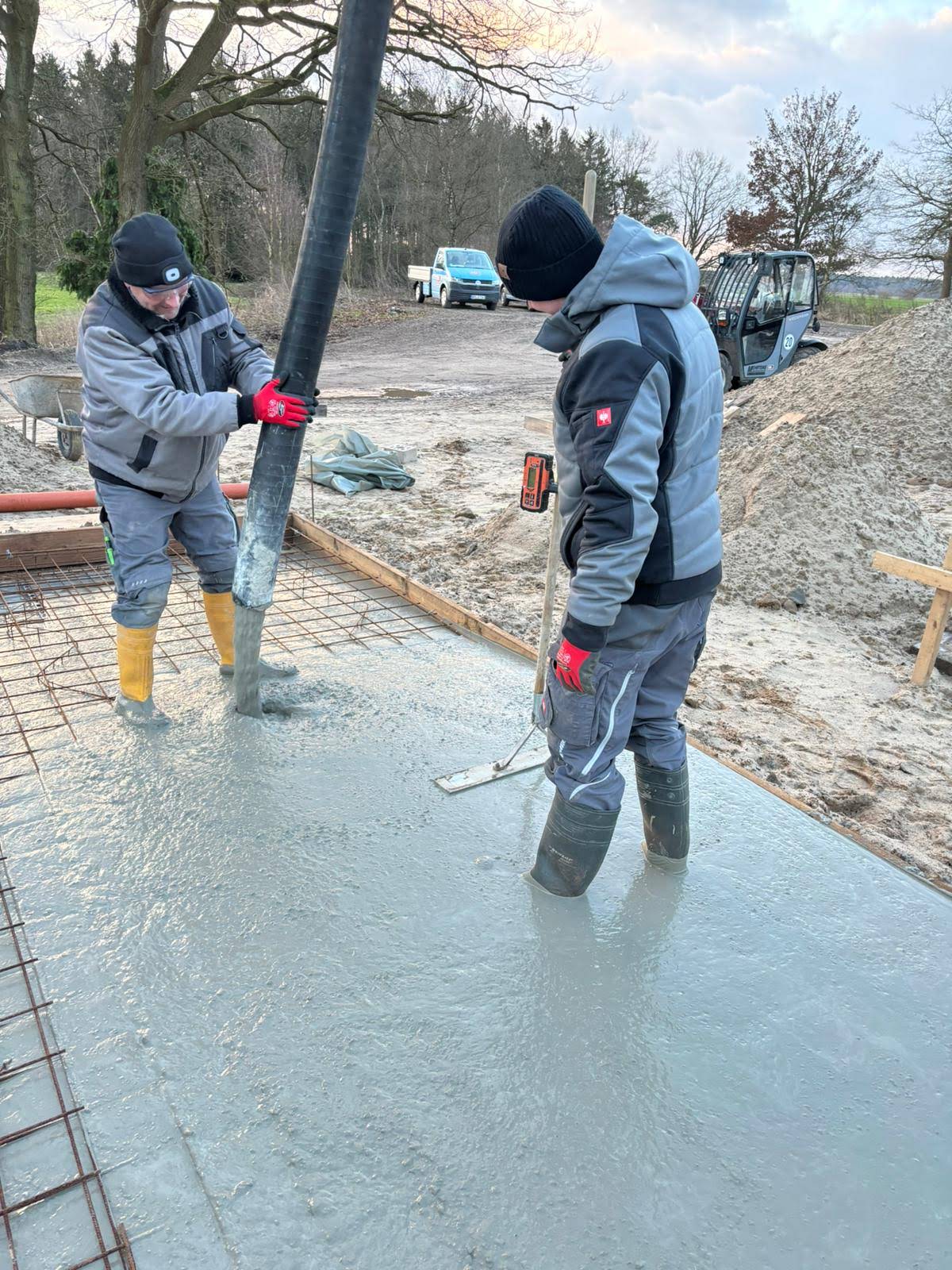 Zwei Bauarbeiter beim Betonieren einer Bodenplatte auf einer bewehrten Schalung mit Fließbeton.